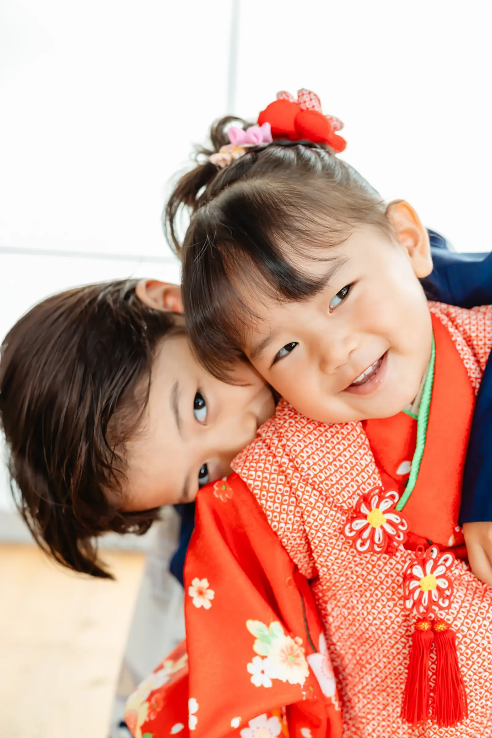 頬を寄せ合う和装のきょうだい、被布の妹と羽織袴の兄の七五三スタジオ撮影