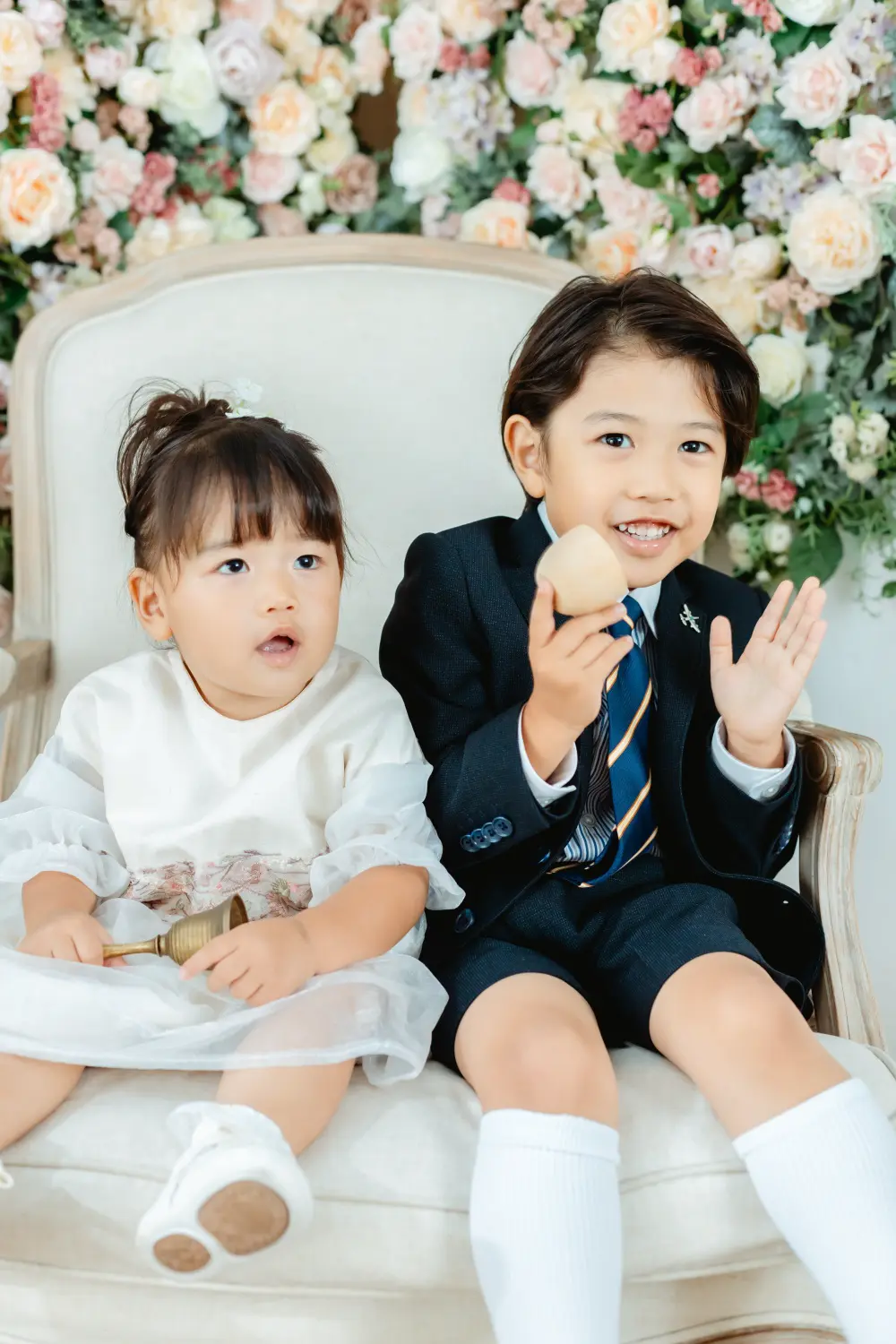 花のバックドロップとアンティーク椅子に座る洋装のきょうだい、七五三スタジオ撮影