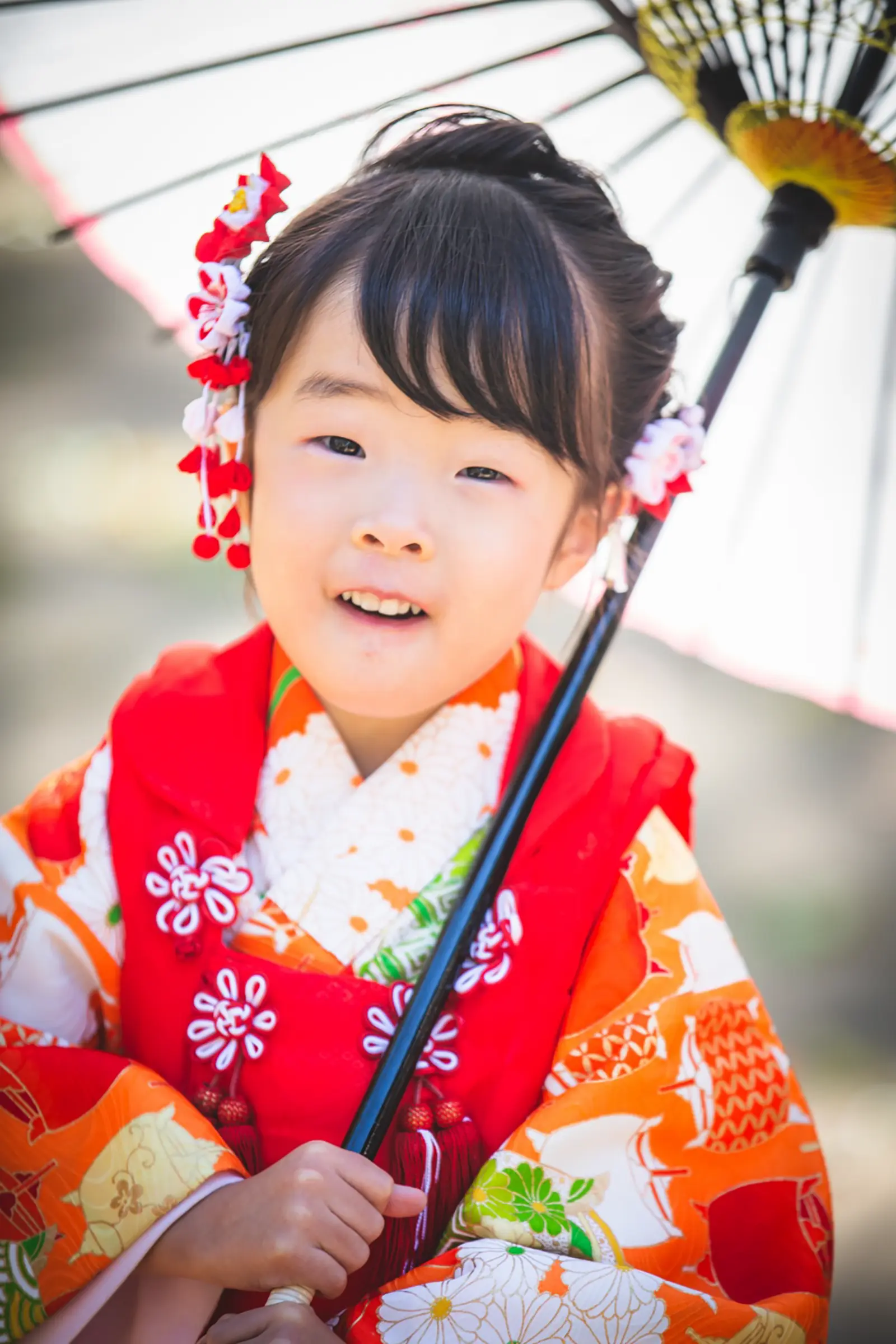 朱赤の被布に赤白のかんざしをつけ、和傘を手にした3歳の女の子の七五三（武田神社・山梨）