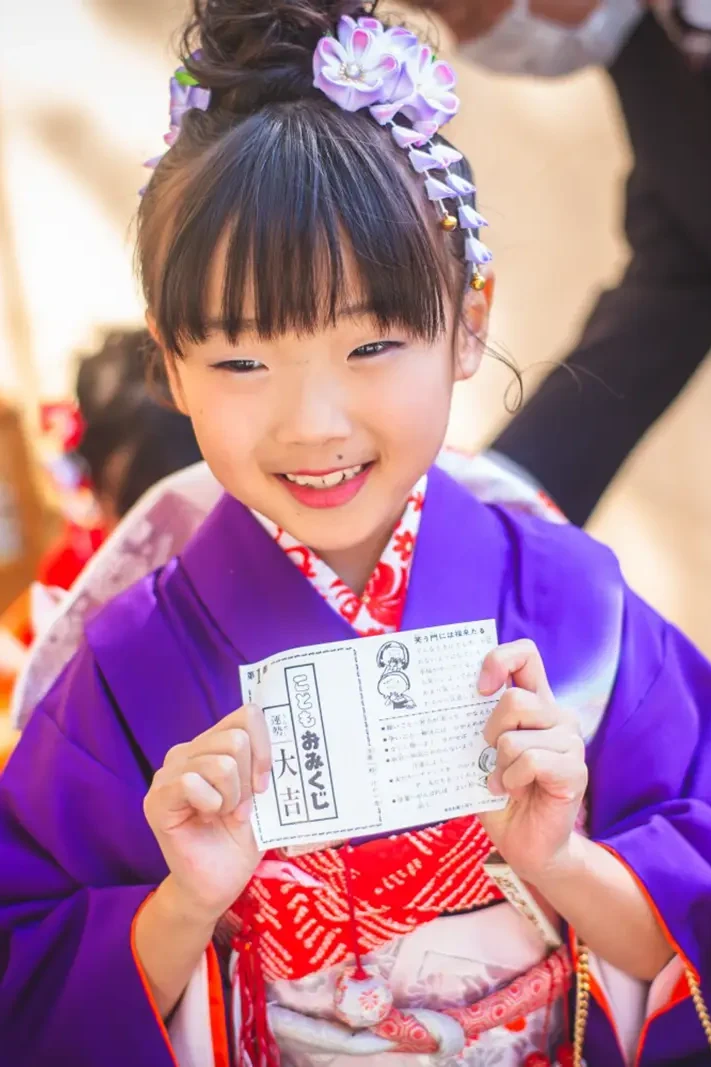 こどもおみくじを両手で掲げて笑う紫の四つ身姿の7歳の女の子、七五三（武田神社・甲府）