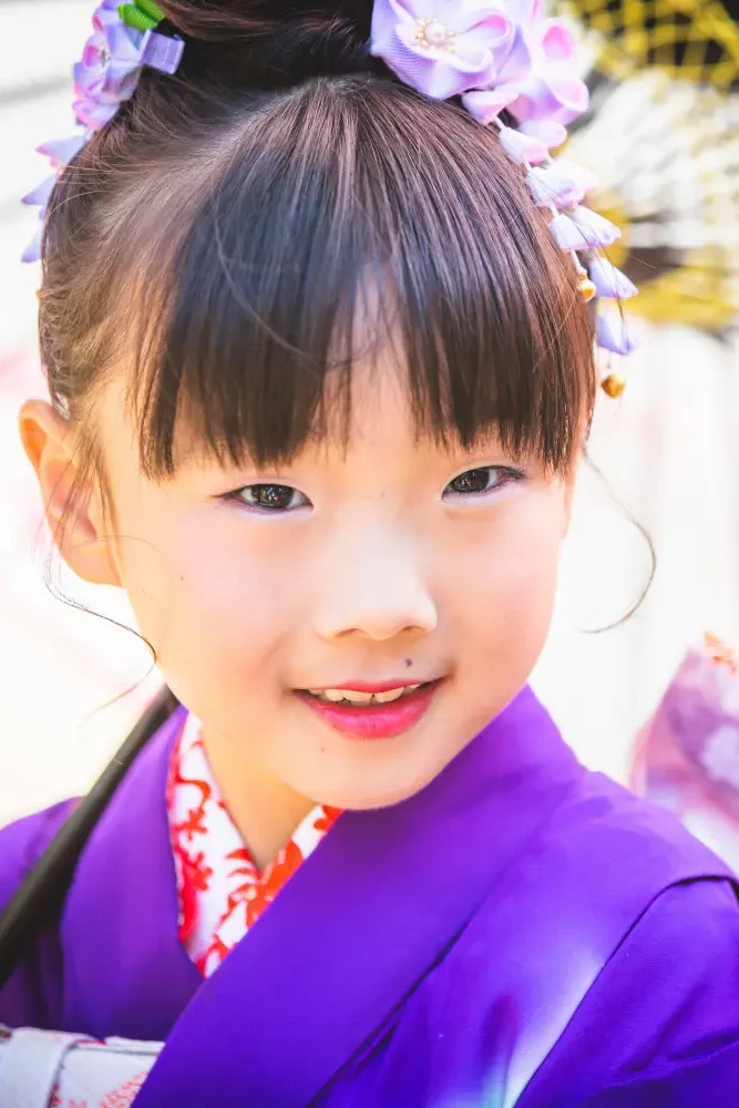 紫の四つ身に紫の花かんざしをつけて微笑む7歳の女の子、和傘を背にした七五三の寄り（武田神社・山梨）