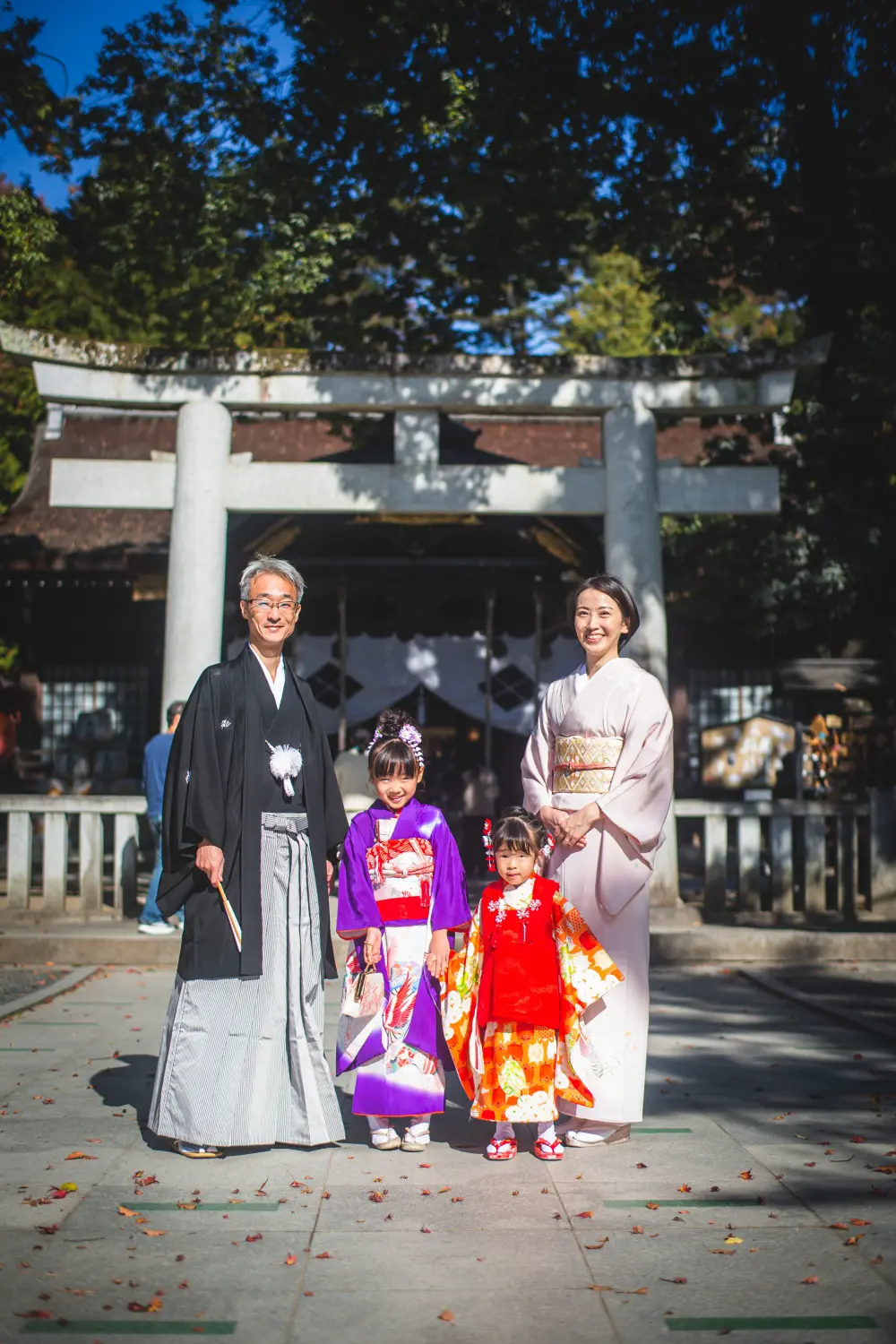 石鳥居と拝殿の前に並ぶ和装の両親と7歳・3歳の姉妹、七五三の家族写真（武田神社・山梨）