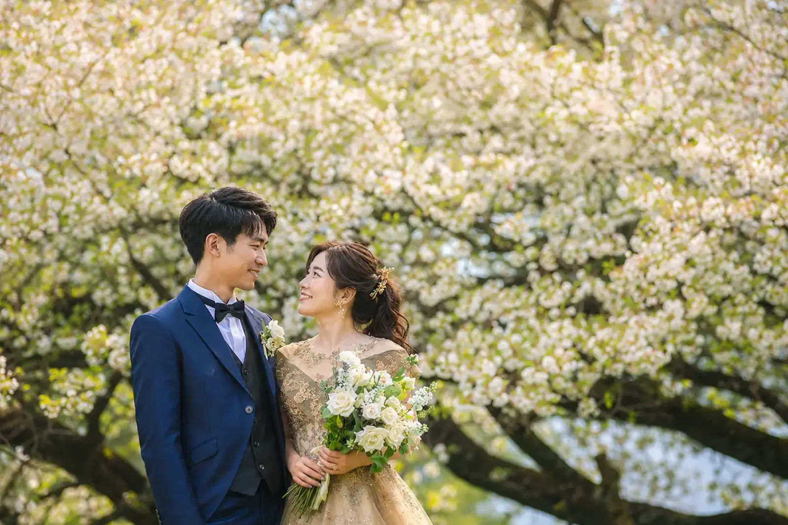 花咲く木を背景に見つめ合う新郎新婦のウェディングフォト