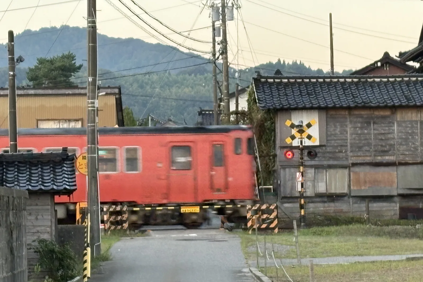 雨晴駅そばの踏切を通る氷見線の赤い列車と古い家並み
