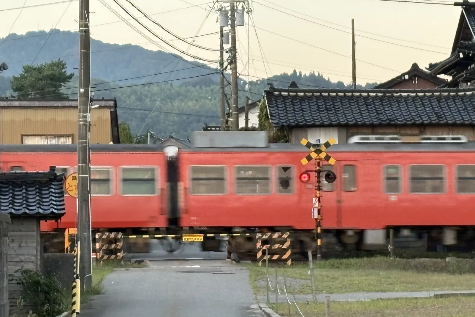 踏切を渡る氷見線の赤い車両と山並み