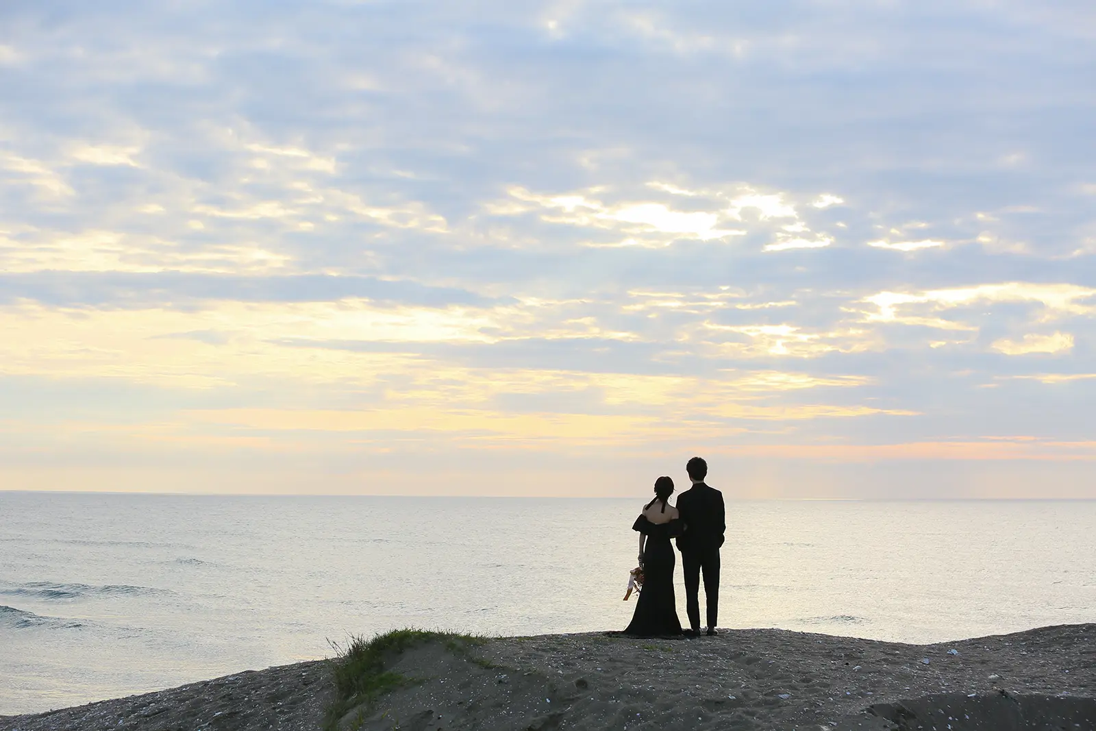 内灘マリーナ周辺の海辺で夕日を背景に手をつなぐ新郎新婦のシルエット写真