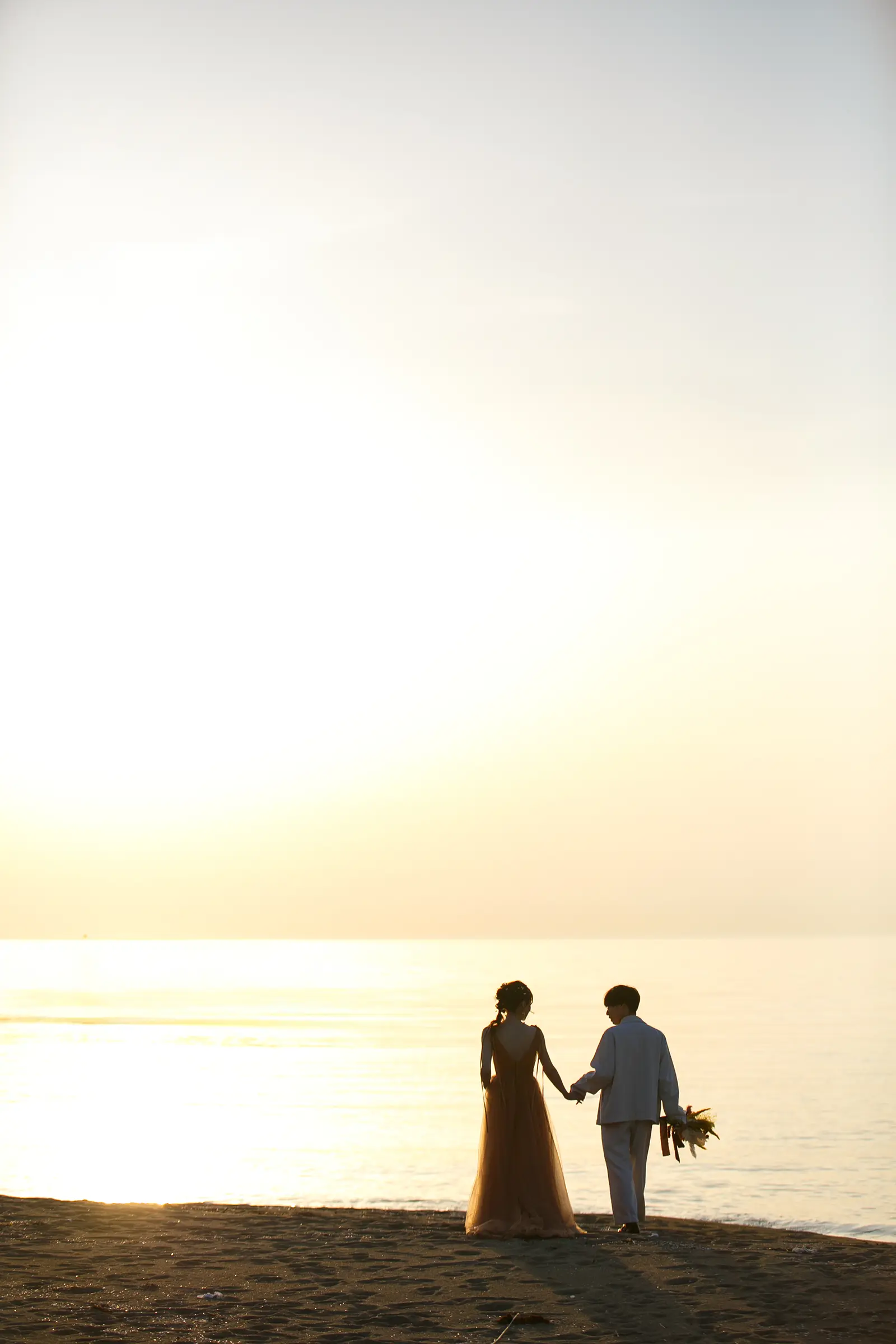 内灘マリーナ周辺の海辺で夕日を背景に手をつなぐ新郎新婦のシルエット写真