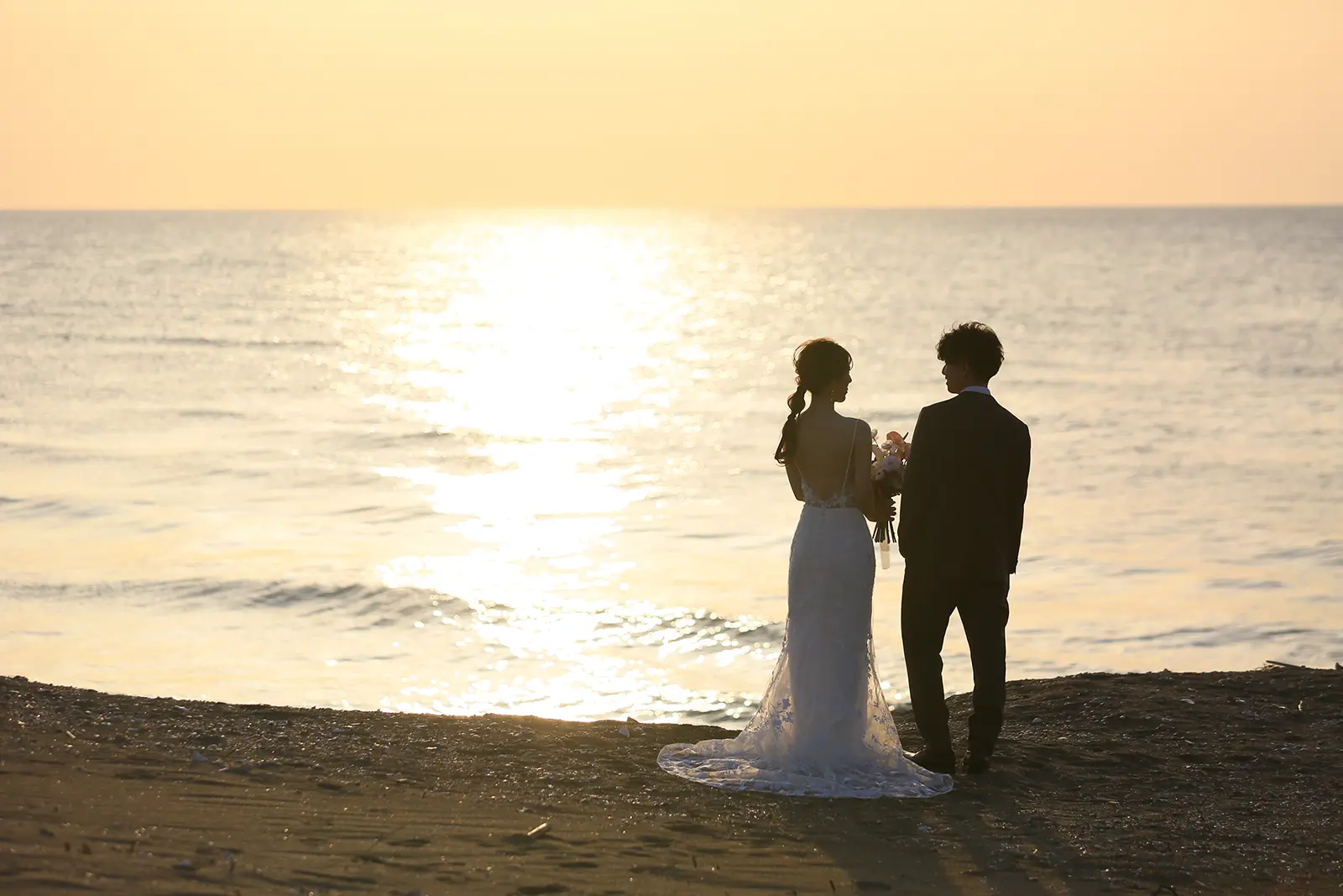 内灘マリーナ周辺の海辺で夕日と海を背景に新郎新婦が向かい合うシルエット写真