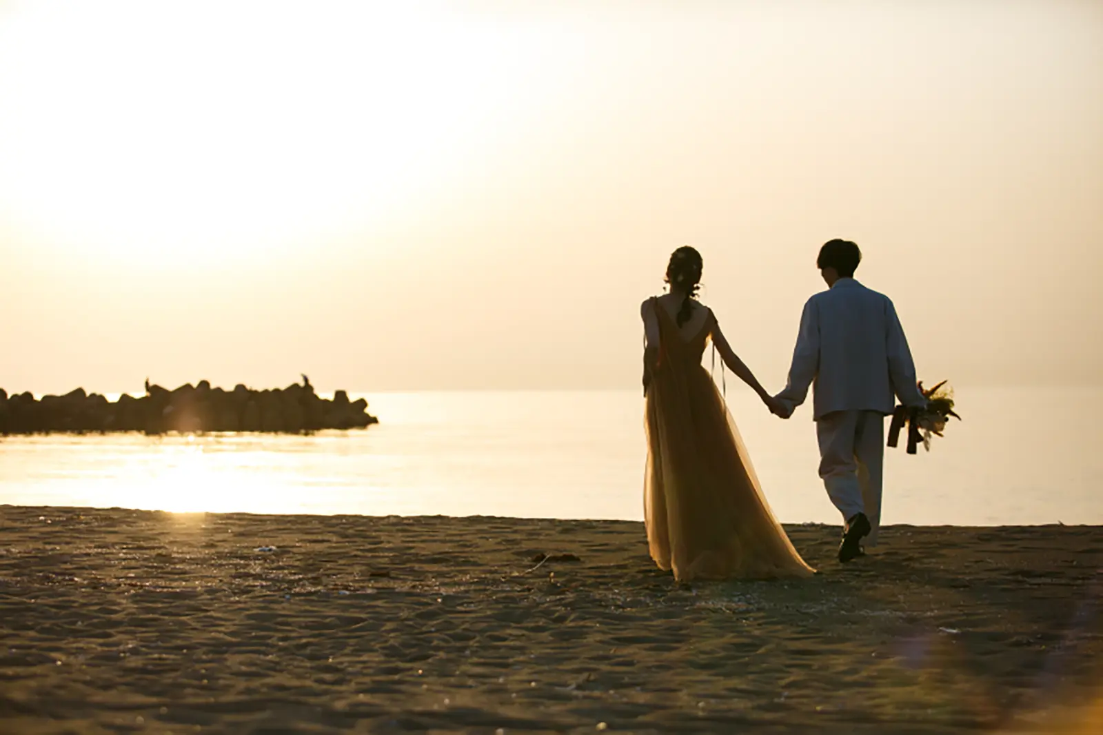 内灘マリーナ周辺の海辺で夕日を背景に手をつないで歩く新郎新婦のシルエット写真
