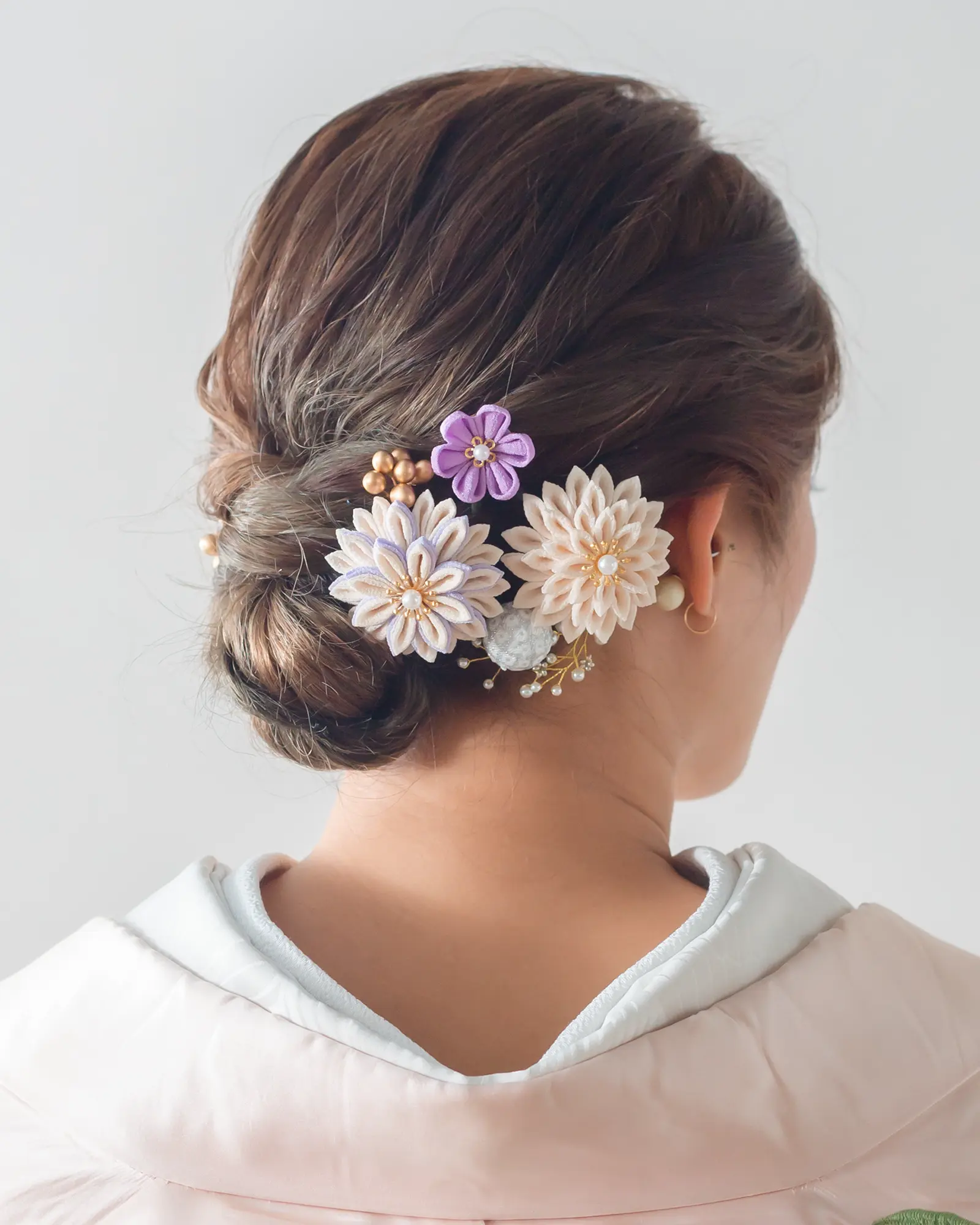 和装に合わせたパステルカラーの花飾りとゴールドアクセントのヘアアレンジ