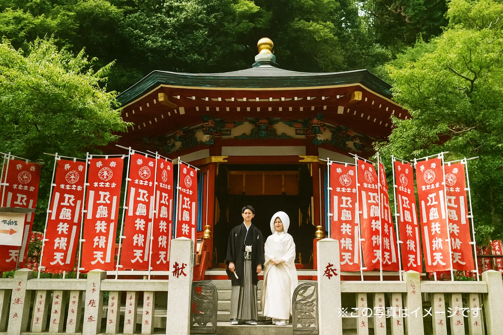 神社の境内にて、白無垢姿の花嫁と紋付袴姿の新郎が並ぶフォトウェディング。新緑と赤い旗が美しい、フォトジェリッシュによる本格的な和装前撮り風景。