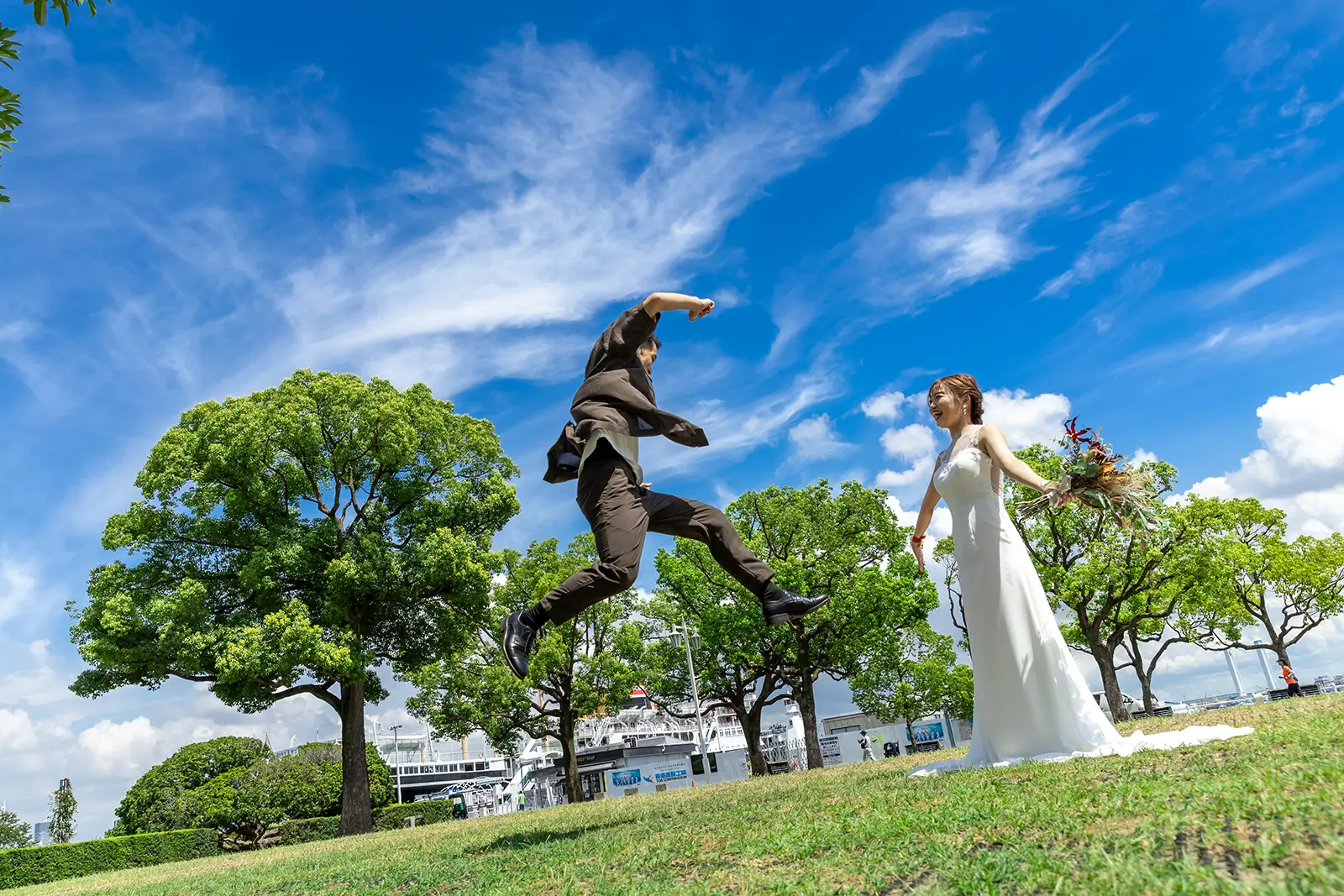 青空の下で新郎がジャンプする山下公園の前撮り写真