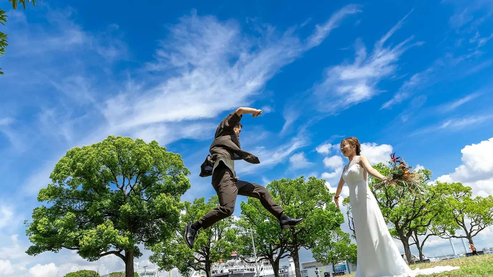 山下公園の青空と緑を背景にジャンプショットを撮るお二人のフォトウェディング