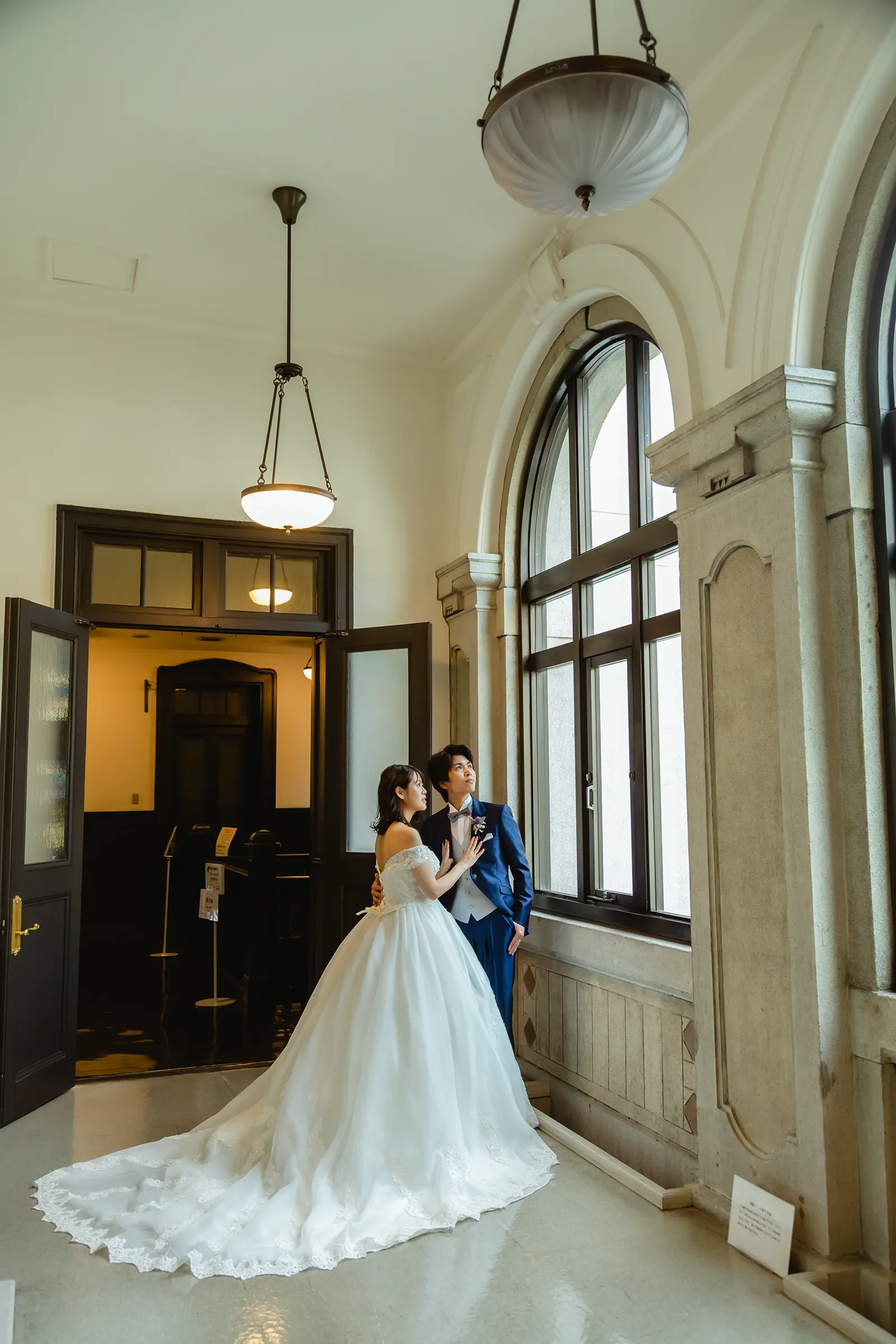 横浜市開港記念会館のアーチ窓のそばに立つ洋装の新郎新婦