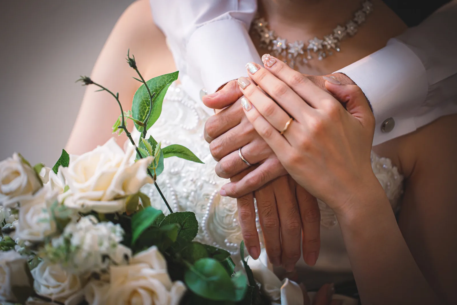 重ねた手と結婚指輪、白いバラのブーケのクローズアップ