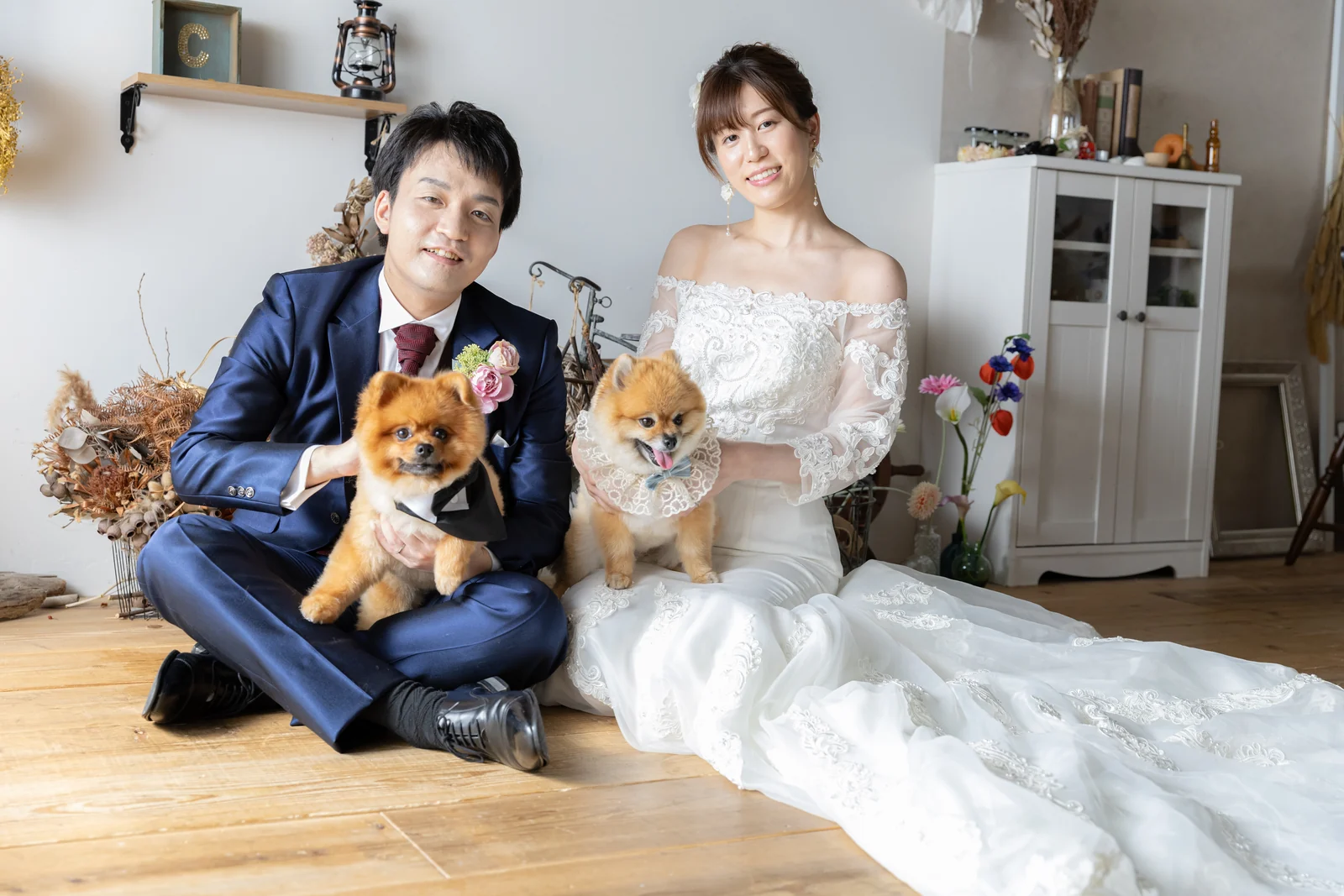 横浜・元町のスタジオでポメラニアン姉弟を膝に乗せて床に座るウェディングドレスの花嫁とタキシードの新郎