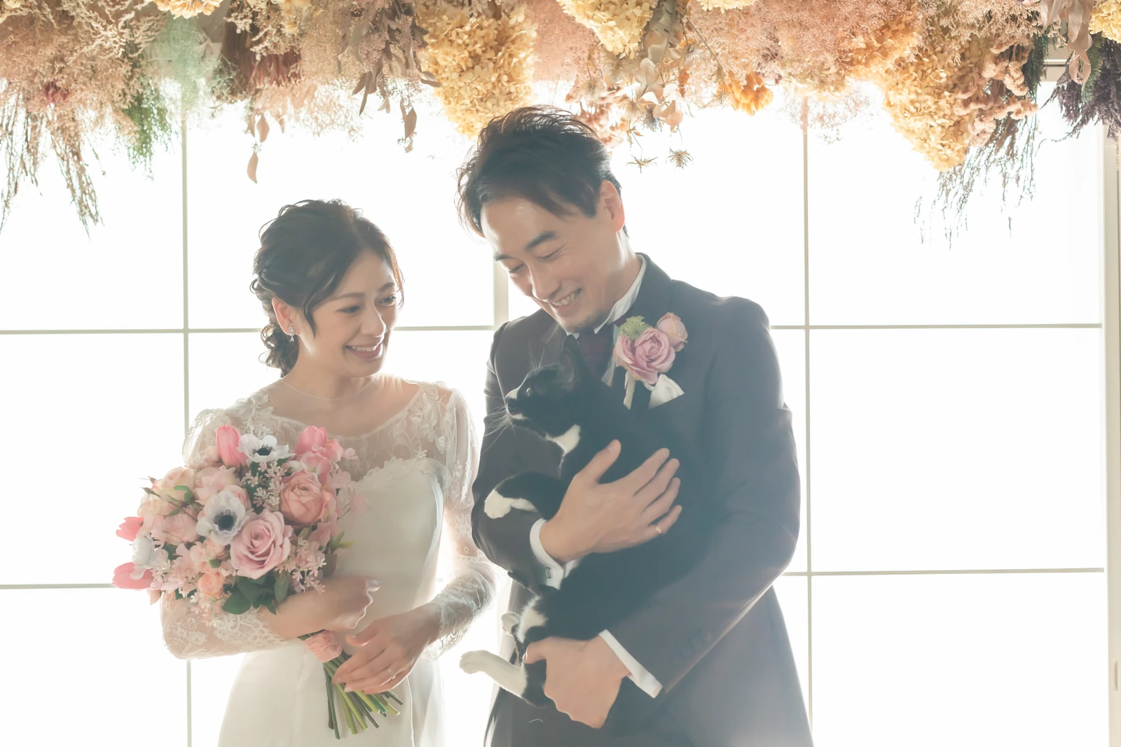 洋装の新郎新婦が黒猫を優しく覗き込むフォトウェディング