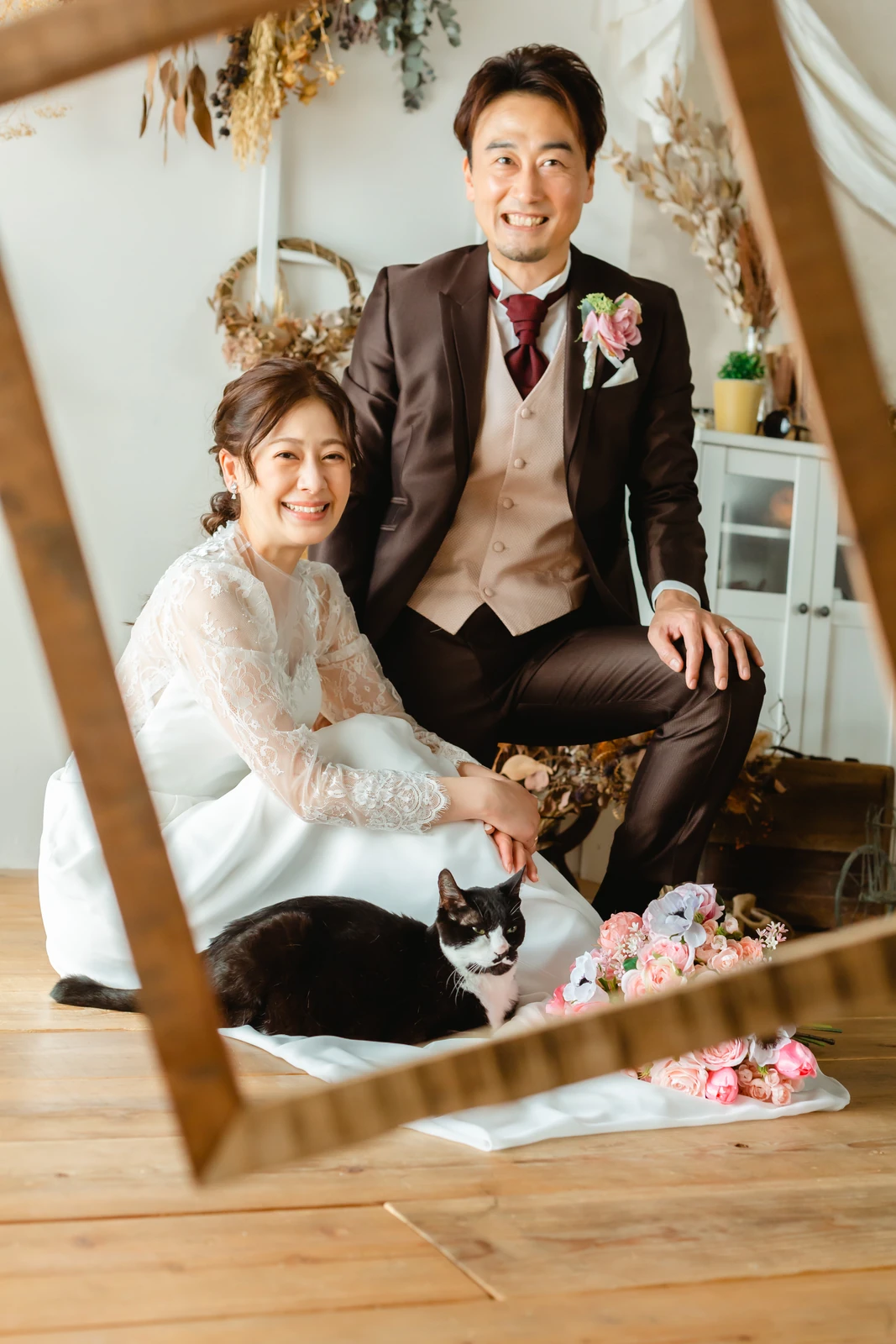 木枠のフレームにおさまる洋装の新郎新婦と黒猫