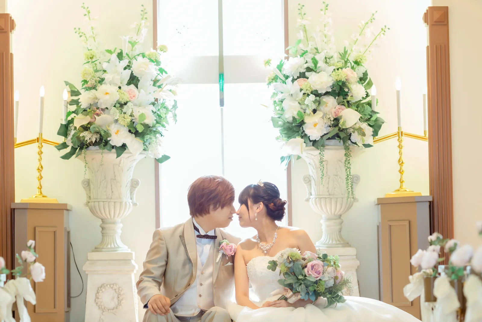 礼拝堂の白い花のスタンドの間でくつろぐ新郎新婦