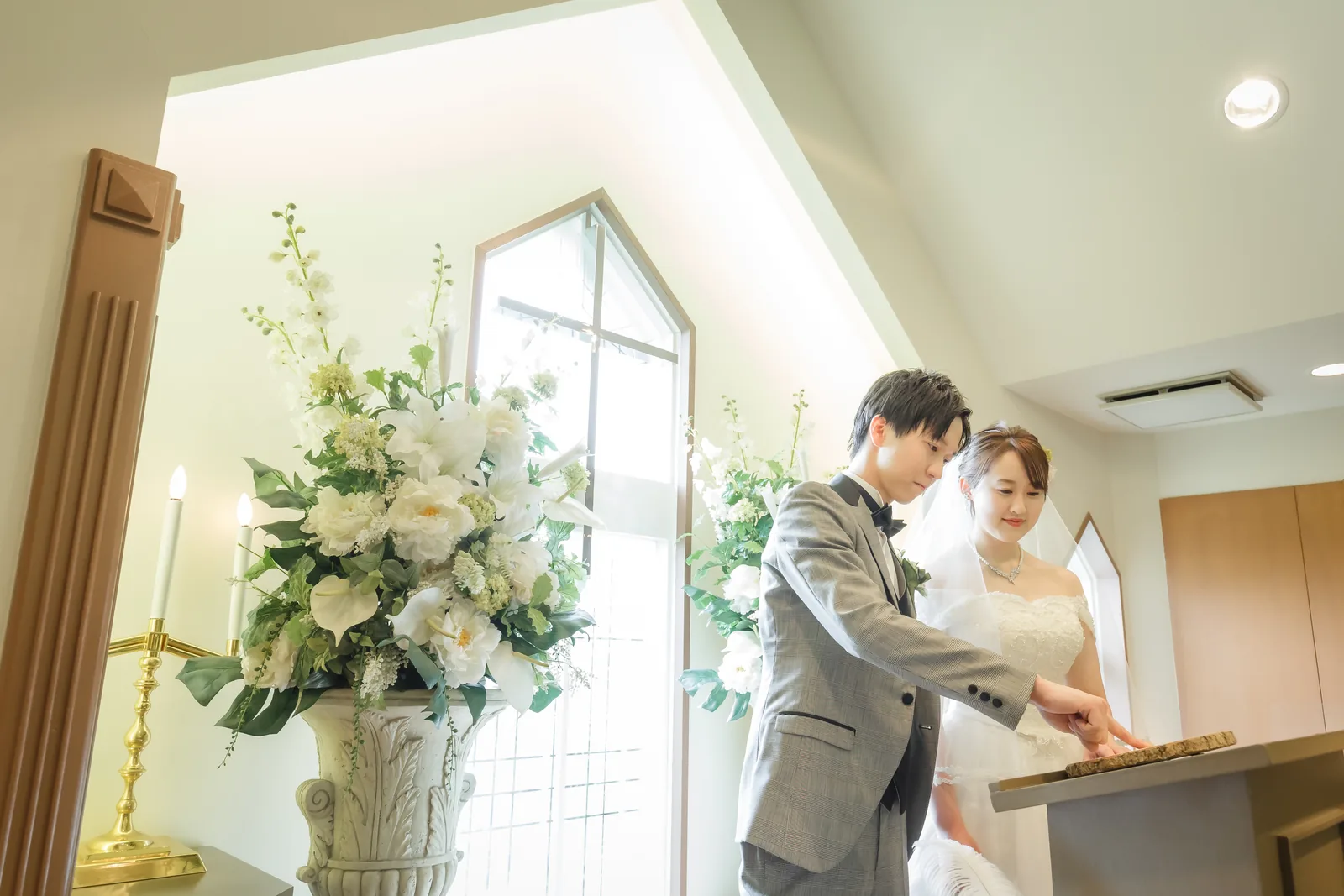 礼拝堂の白い装花のそばで寄り添う新郎新婦