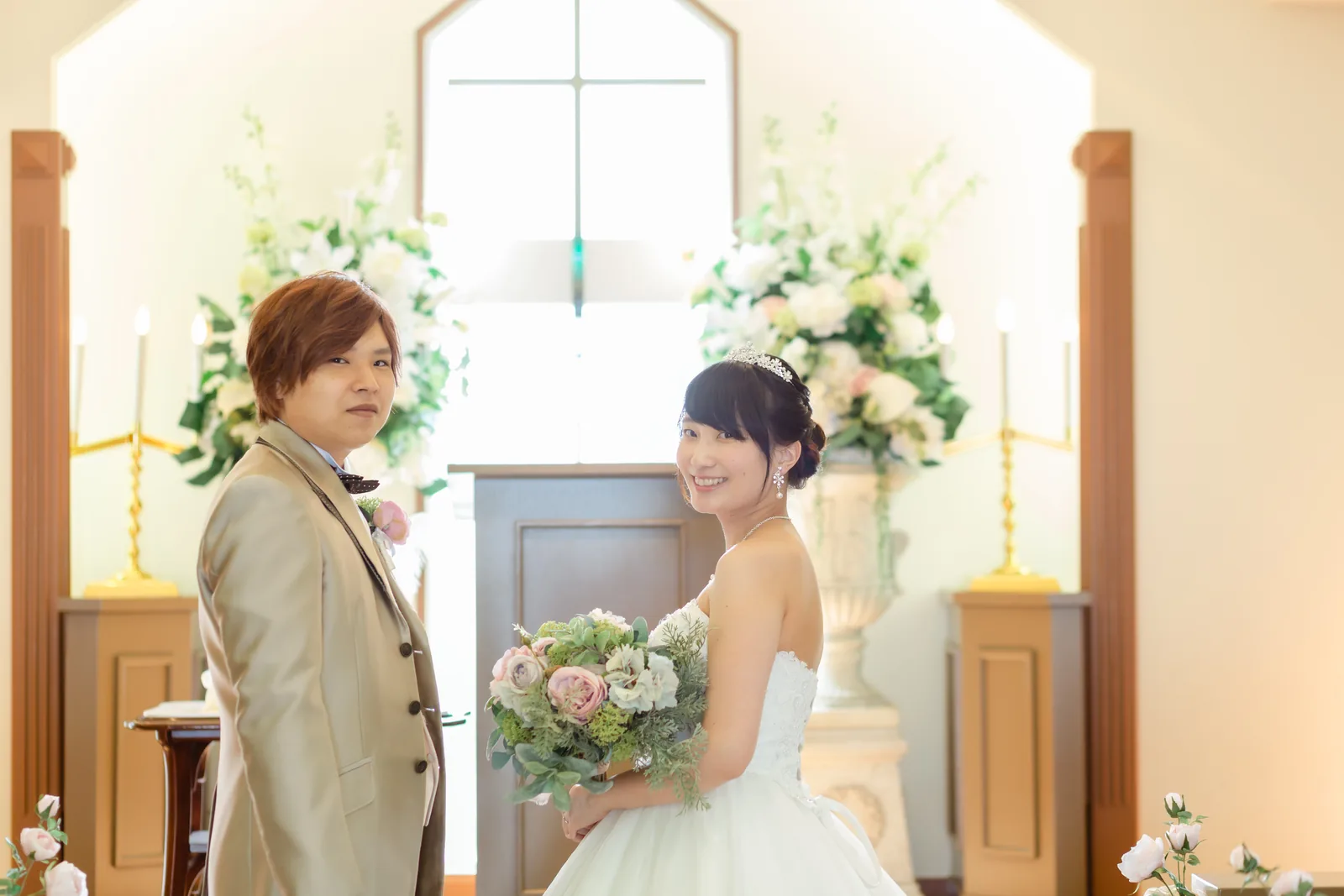 礼拝堂の花のスタンドの前で笑い合う新郎新婦