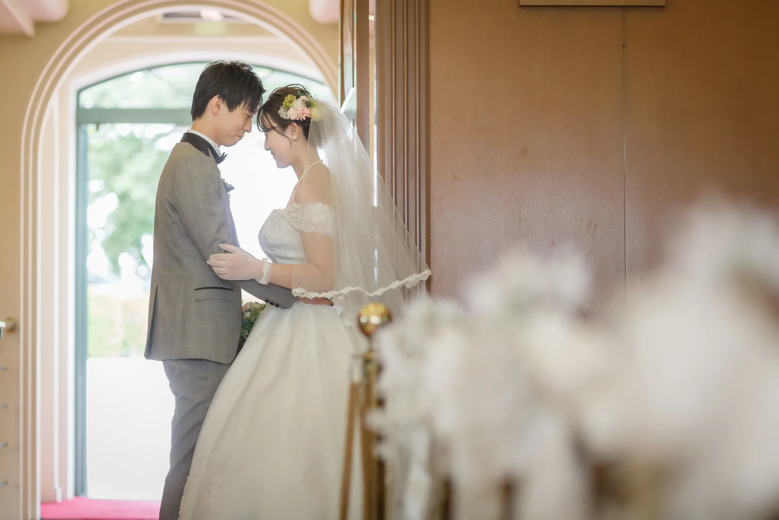 白い花を前景にして額を寄せ合う新郎新婦のウエディングフォト