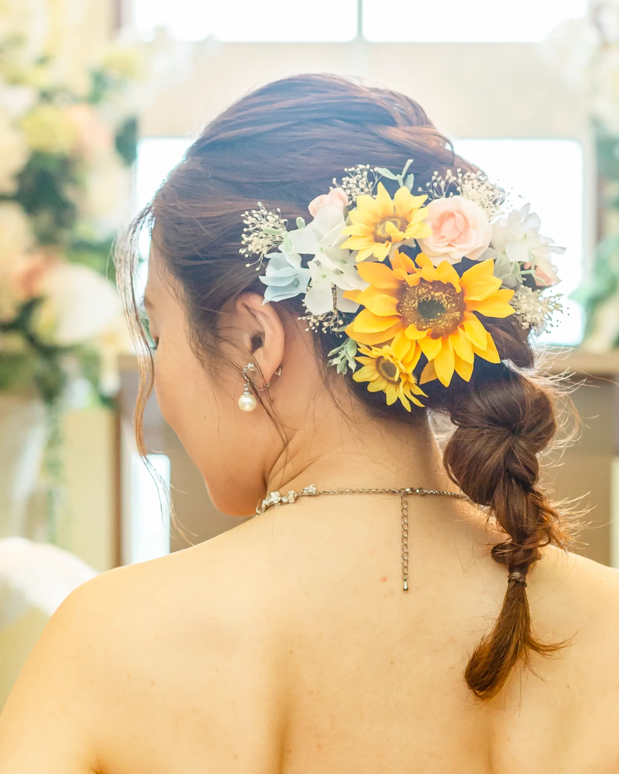 洋装のロングヘアを編みおろしにまとめ、ひまわりの髪飾りを合わせた花嫁ヘアスタイル