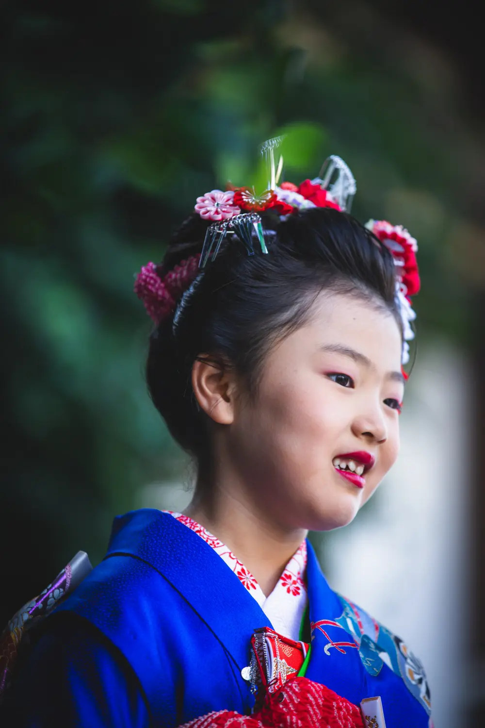 日本髪風の結い上げに赤い花かんざしをつけて笑う7歳の女の子の横顔、七五三（湯島天神・東京）