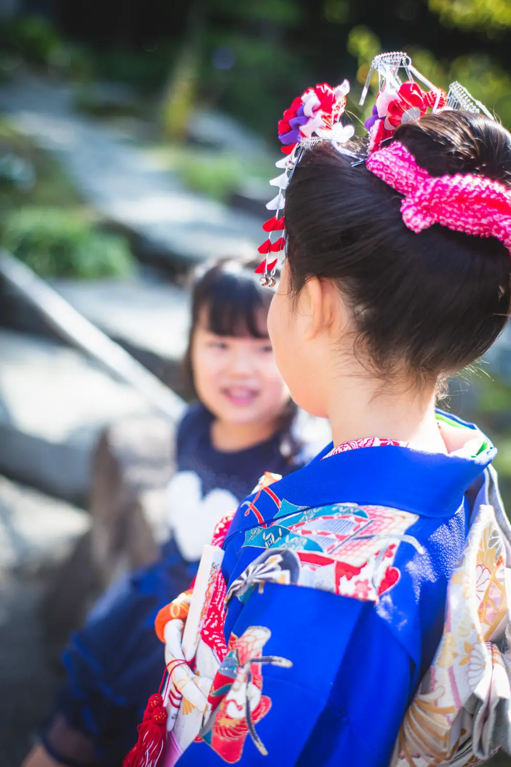 7歳の女の子の後ろ姿ごしに笑う妹、七五三の家族撮影（湯島天神・東京）