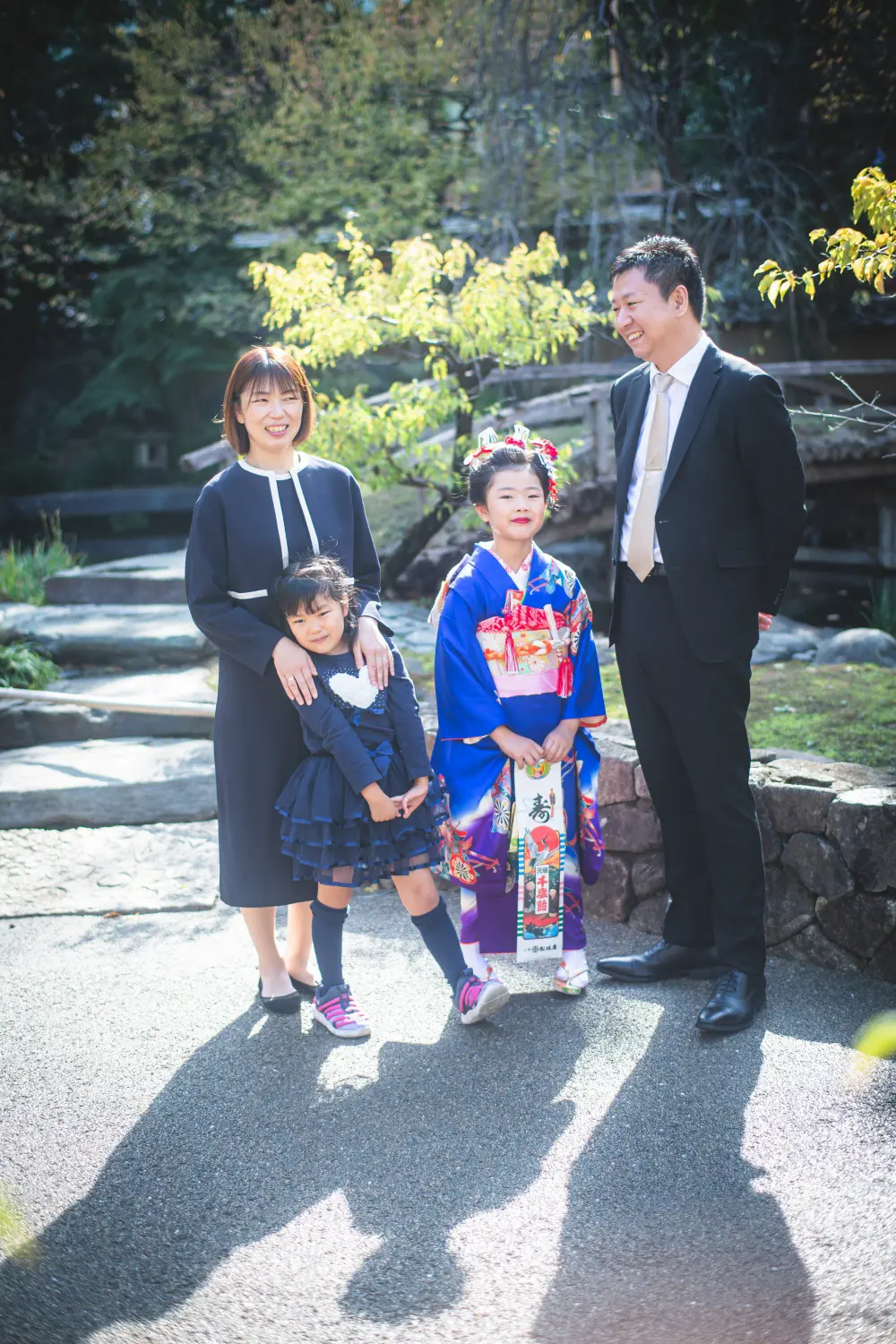 庭園で並ぶ父・母・妹と四つ身姿の7歳の女の子の家族写真、七五三の出張撮影（湯島天神・東京）