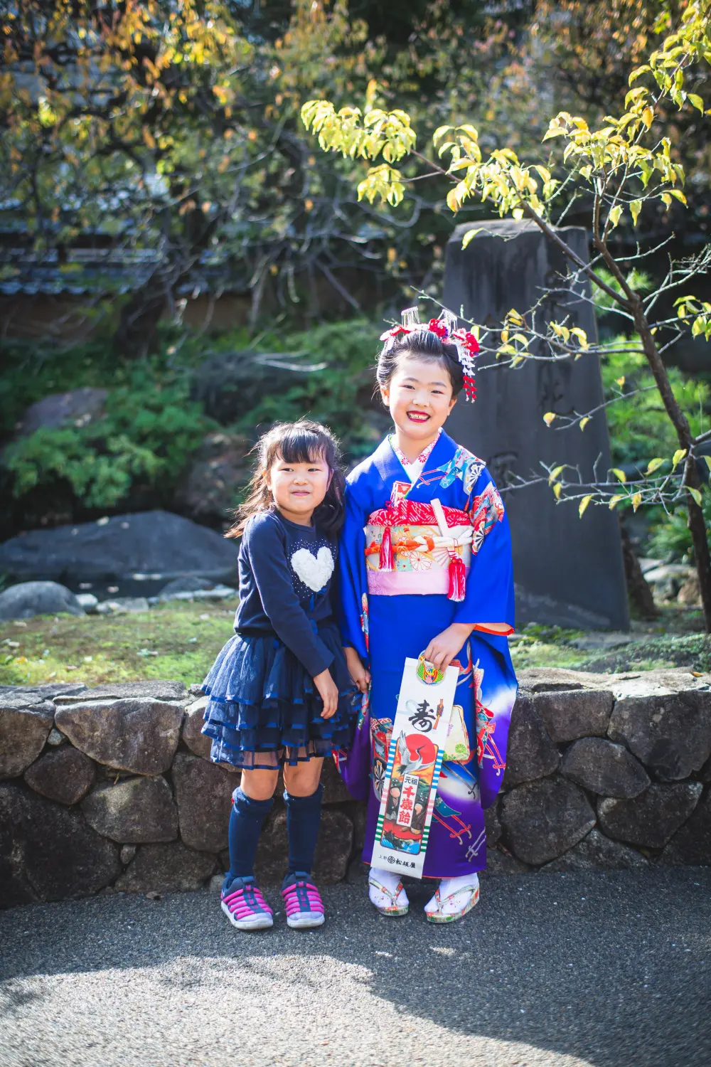 石碑の前に並ぶ四つ身の7歳の女の子と洋服の妹の全身、七五三（湯島天神・東京）